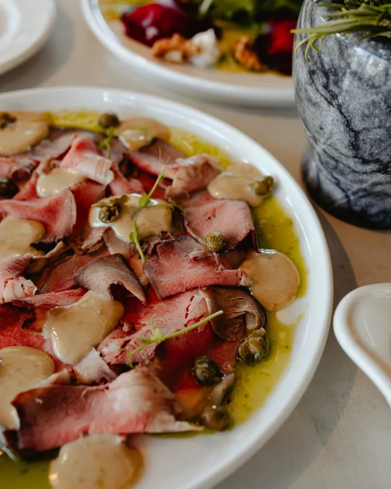 Thinly sliced meat with capers and sauce, on a white plate