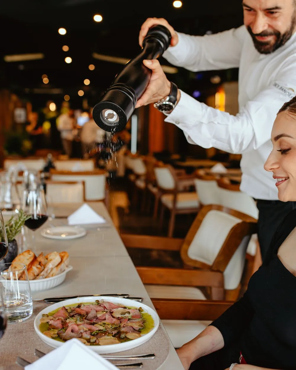 Chef grinding pepper over a guest's plate