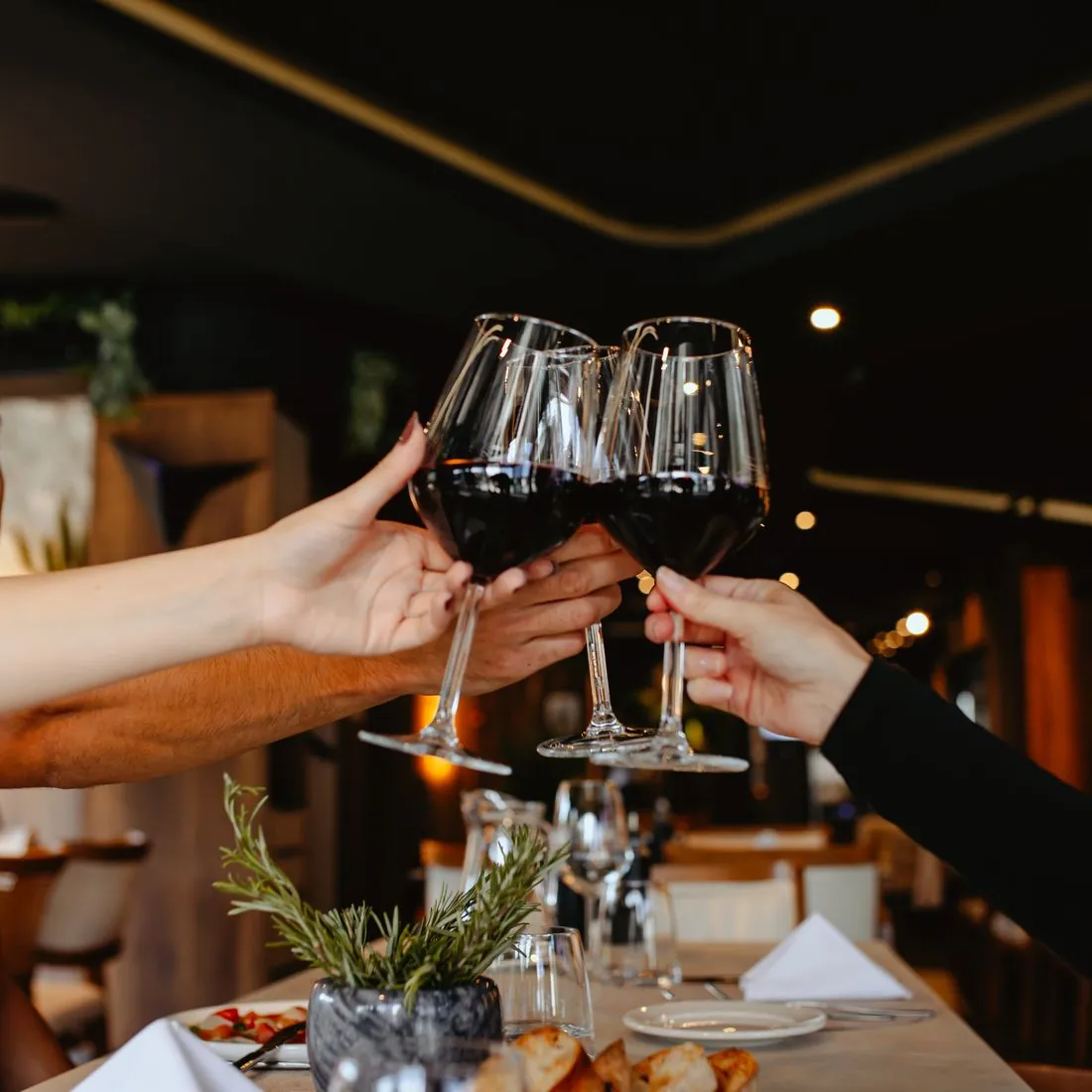 Four glasses of red wine raised in a toast above the table